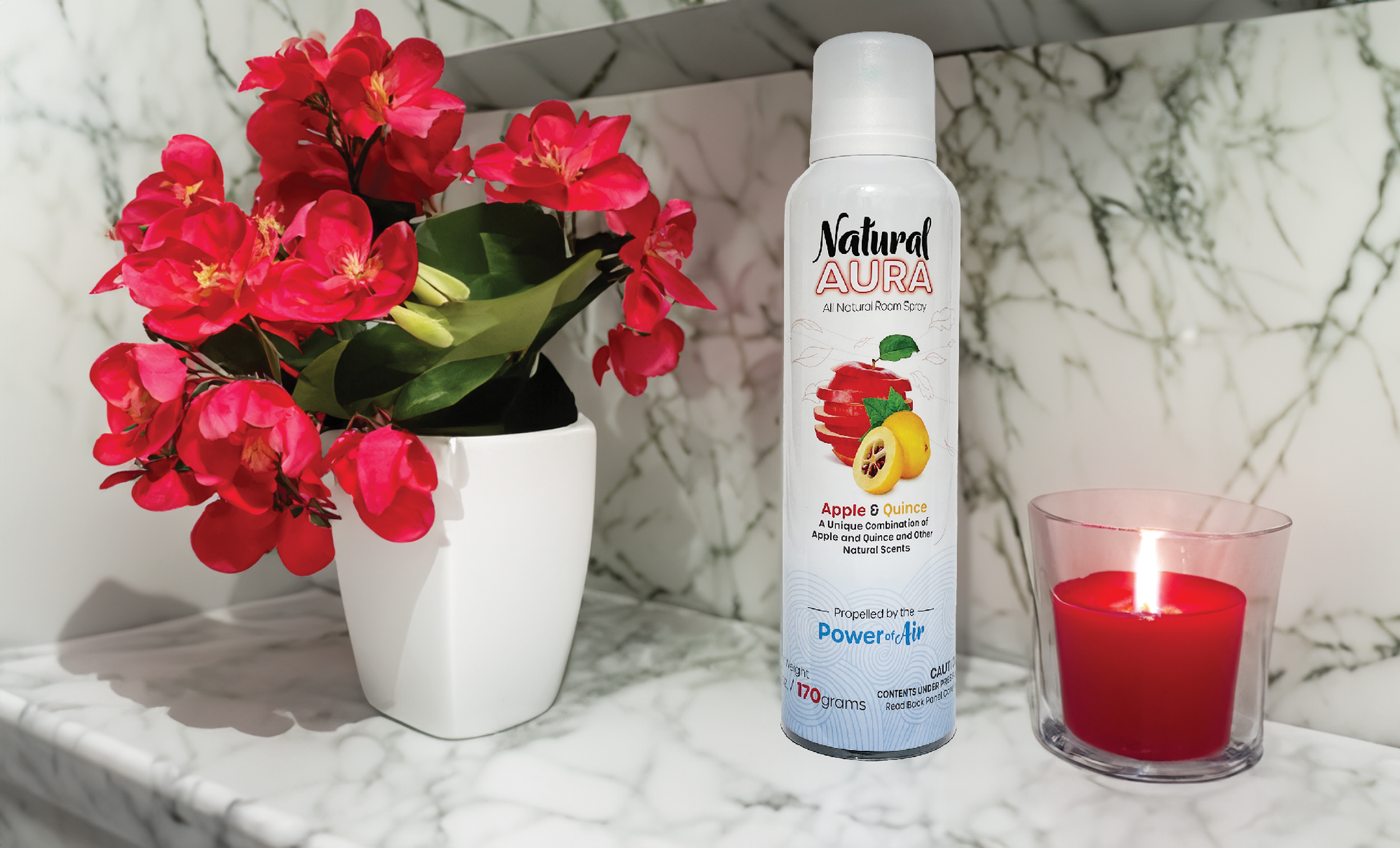 Natural Aura Apple and Quince Room Spray sitting on a bathroom white and black marble counter with red flowers and a red lit candle.