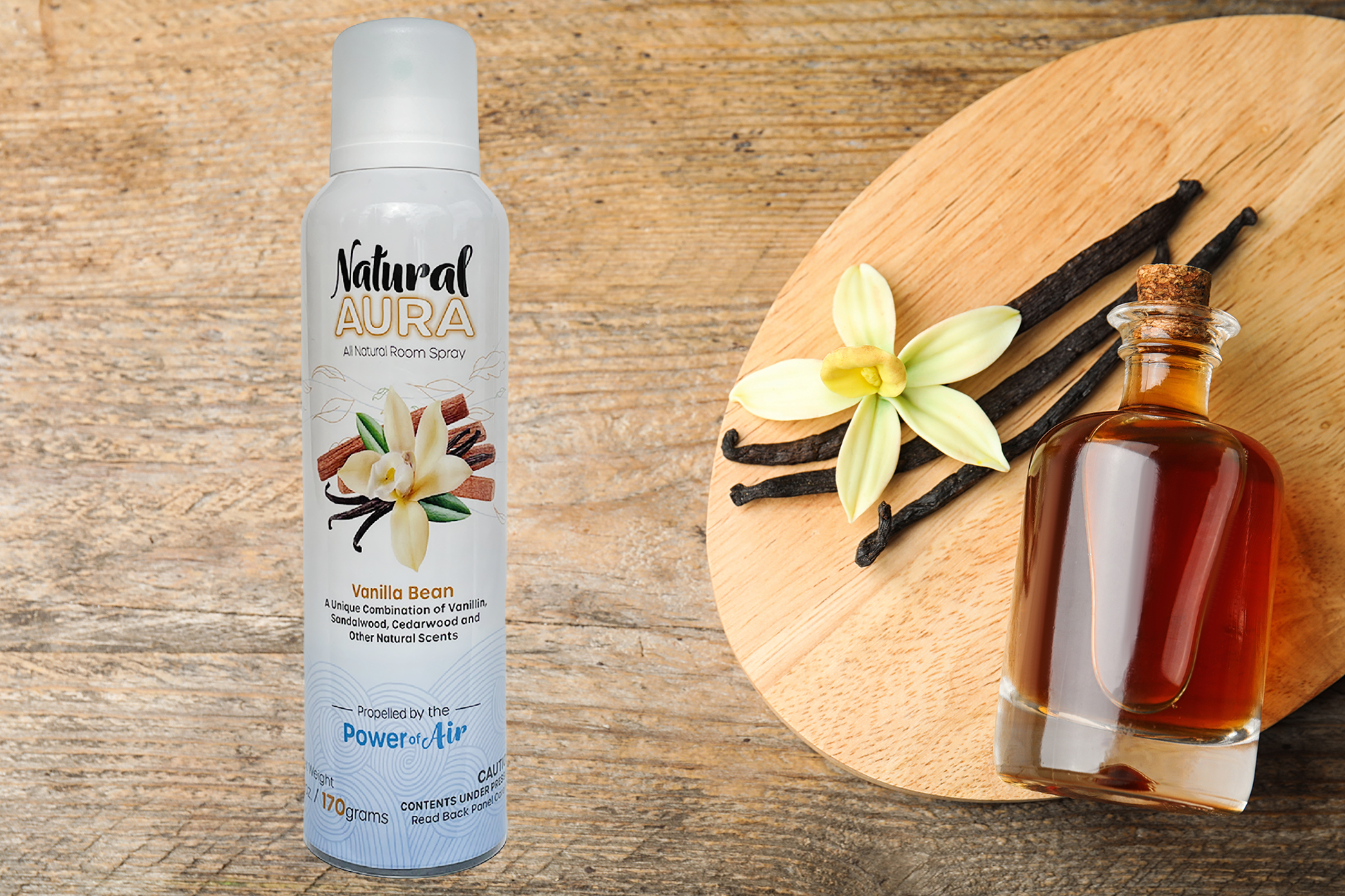Bottle of Natural Aura Vanilla Bean Room Spray on a tan wooden table with vanilla bean sticks and vanilla extract oil in a clear glass bottle with a cork top.