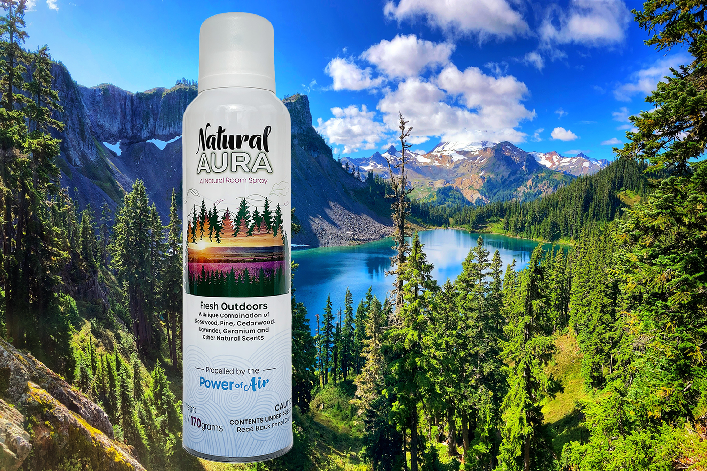 Bottle of Natural Aura Fresh Outdoors room spray with a mountain with a blue sky background that includes a blue lake and pine trees.